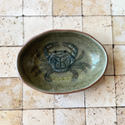 Green ceramic bowl with crab design on a tiled wall