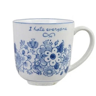 A white ceramic coffee mug with a blue floral pattern and the text 'I hate everyone' printed in blue script near the rim.
